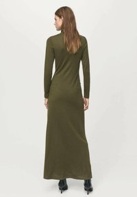 Vestido maxi de manga larga en verde oliva con silueta ajustada, textura acanalada y cuello redondo, combinado con botas de tacón.