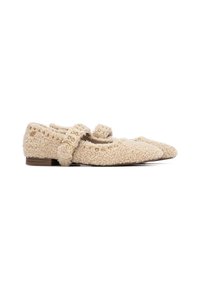 Mocasines texturizados beige con parte superior de tela suave, puntera afilada y una correa decorativa con tachuelas doradas, colocados sobre un bajo tacón de madera.