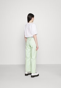 T-shirt branca cortada combinada com calças longas e largas verdes com um padrão ondulado, realçadas com um cinto preto e sapatilhas brancas.