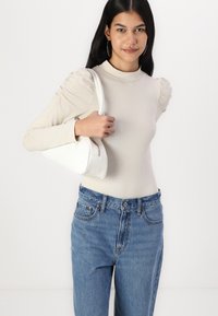 Beige dlhý rukáv top so zberanými ramennými časťami, skombinovaný s svetlomodrými vysokými džínsami a bielou trojuholníkovou kabelkou.