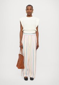 Bela rebrasta pletena brezrokavna majica, večbarvne prugaste široke hlače, rjav pletena torba in črne ravne čevlje.