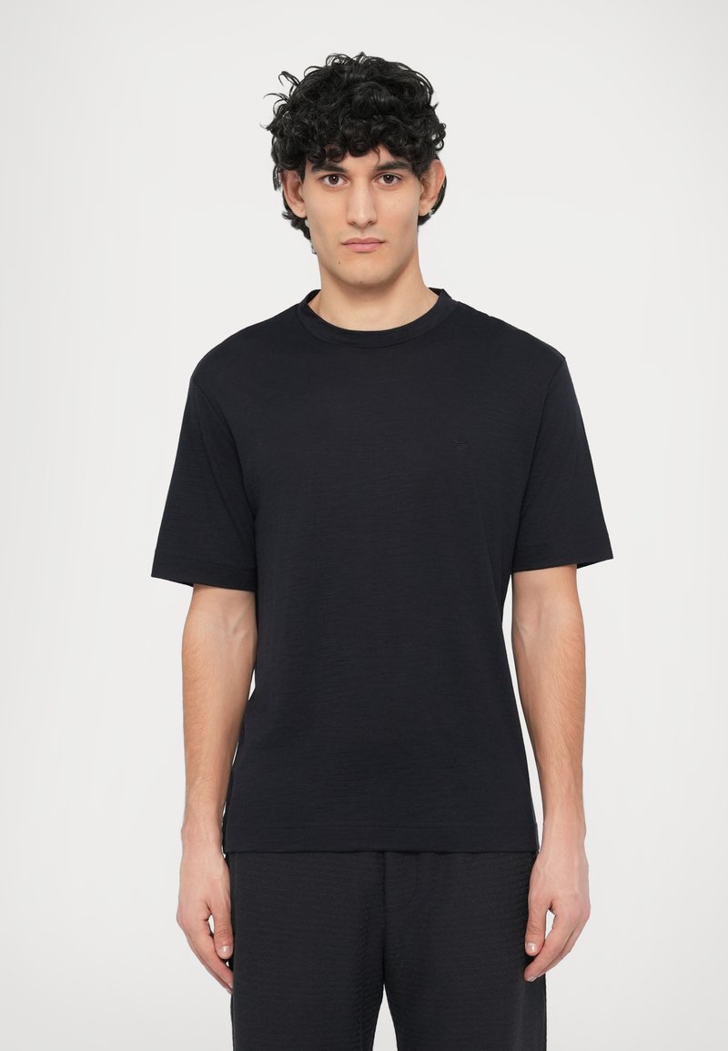 Fekete rövid ujjú póló kerek nyakkivágással, puha anyagból készült, minimalista dizájnnal, apró logó részlettel a mellrészen.