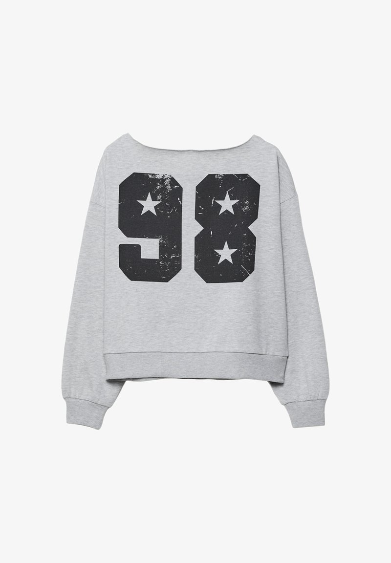 Šedý zkrácený svetr s černým opotřebovaným potiskem obsahujícím číslo "98" a dvě černé hvězdy na zadní straně. Dlouhé rukávy, ležérní design.
