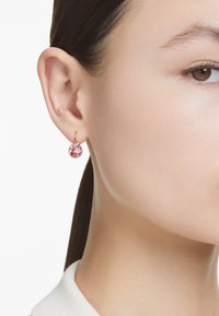 Brinco de argola em ouro rosa com uma pedra preciosa redonda e rosa no centro. Acabamento metalizado suave, design pequeno e pendente.