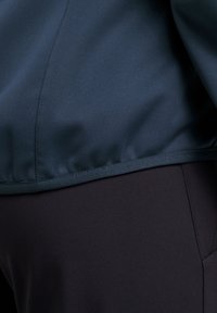 Donkerblauwe jaszoom over zwarte broek met zichtbare naden en gladde stoftexturen in een close-upweergave.