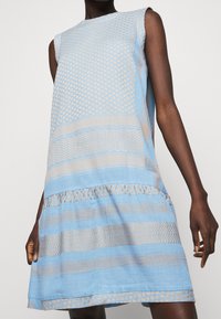 Hellblaues ärmelloses Kleid mit unterschiedlichen Texturen und Streifen, einem gestuften Saum und subtilen beige Akzenten.