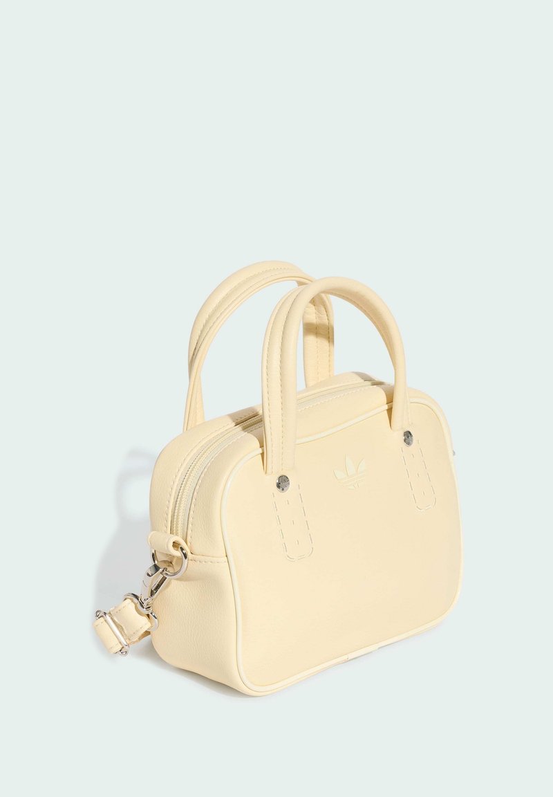 Piccola borsa color crema con doppi manici, chiusura con zip in alto, tracolla staccabile e logo Adidas in rilievo sul davanti.