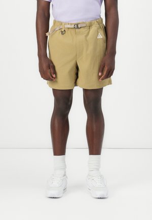 Beige shorts with an elastic waistband and adjustable drawstring, featuring a small logo on the left side and a relaxed fit.