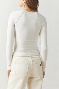 Långärmad, ribbad topp i krämfärg med spetsdetaljer vid halsringningen, kombinerad med ljusa jeans som har bakfickor och en liten etikett.