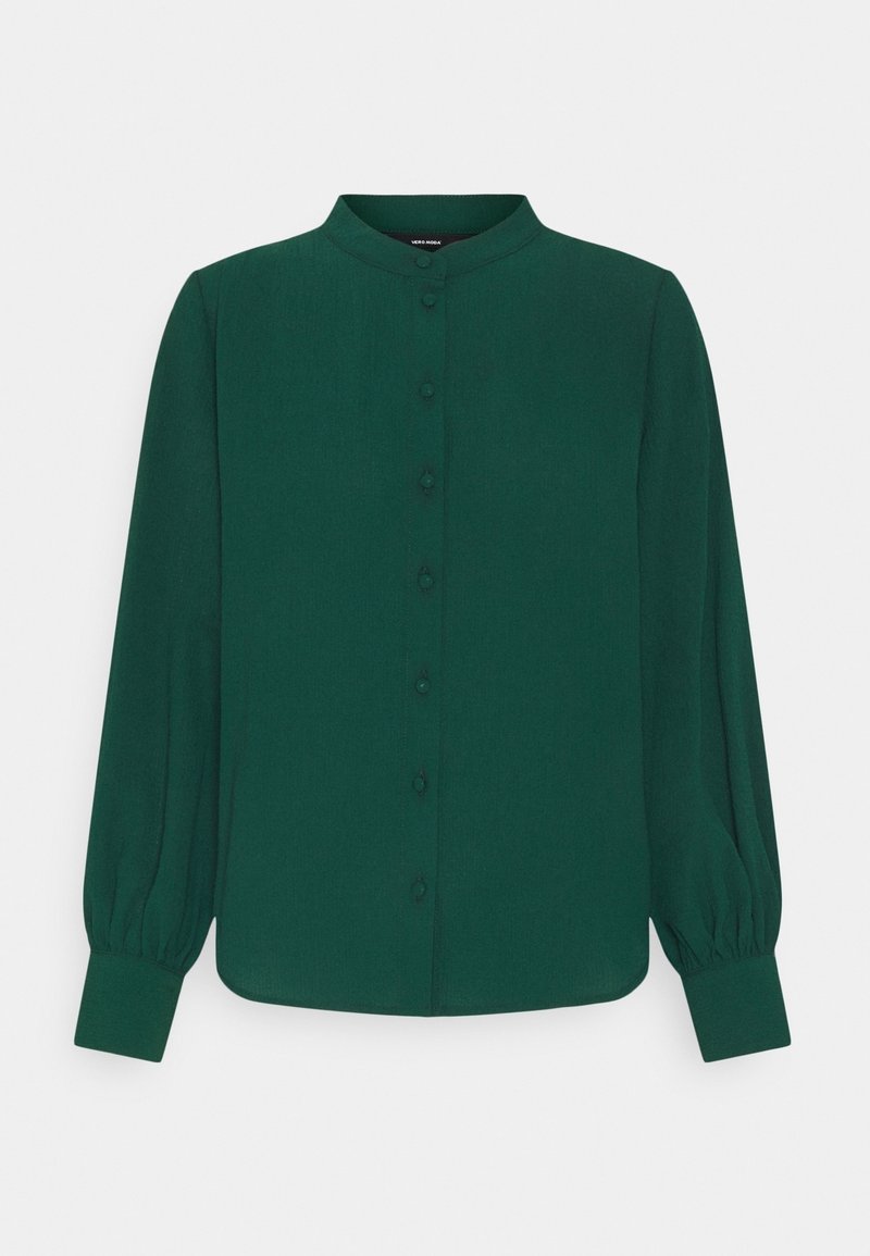 Blouse verte foncée à manches longues avec col rond, devant boutonné et poignets froncés sur un fond clair uni.