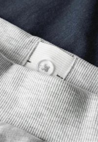 Valge nööbi lähivõte, mis on kinnitatud heledahalli rõiva sooniliste vöökohal tumedal kangapõhjal.