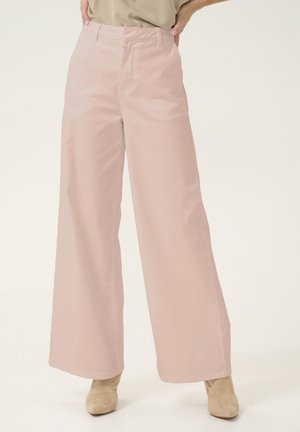 Pantalons larges rose clair en tissu lisse, avec une taille haute et des poches avant, assortis à des bottines beige.