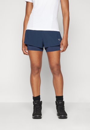 Pantaloni corti blu navy con un design a strati, dotati di una fodera interna. Abbinati a stivali da trekking neri e testurizzati e calze scure.