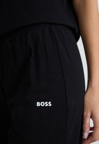 Mustat puuvillaiset jogger-housut, joissa on joustava vyötärö ja valkoisella painettu "BOSS"-logo alahänessä. Kangas on pehmeä ja sileä.