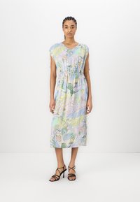 Blomstermønstret midi-kjole i pastellfarger, med v-hals, korte ermer, innsnørt midje og lett stoff. Brukt med svarte stroppesandaler.