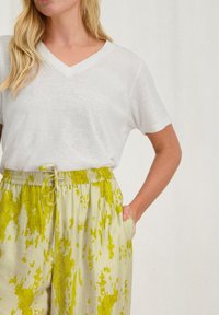 Witte T-shirt met korte mouwen en V-hals, gecombineerd met lichte, gebloemde broek met trekkoorden in geelgroene tinten. Gestructureerde, ontspannen pasvorm.