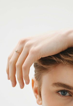 Anillo de plata delicado con una pequeña gema, usado en el dedo anular. La mano descansa suavemente sobre el cabello, mostrando un tono de piel suave y uñas naturales.