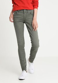 Olivgrønn skinny jeans med en jevn tekstur, fem-lommedesign og kontrasterende sømmer, kombinert med hvite joggesko.