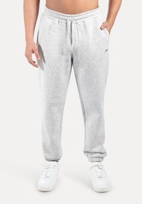 Ljusgrå mjukisbyxor med elastisk midjeband och dragsko, utrustade med sidofickor och avsmalnande muddar. Kombinerade med vita sneakers.