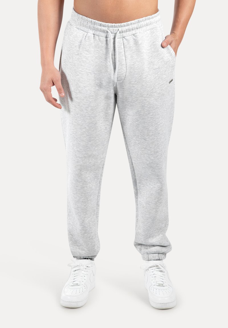 Ljusgrå mjukisbyxor med elastisk midjeband och dragsko, utrustade med sidofickor och avsmalnande muddar. Kombinerade med vita sneakers.