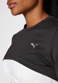 Schwarzes und weißes Sportoberteil mit rundem Ausschnitt, featuring ein graues Puma-Logo, hergestellt aus glattem, leichtem Gewebe mit kontrastierenden Farbblöcken.
