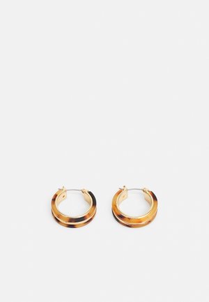 Petites boucles d'oreilles créoles avec détails dorés et motif écaille sur fond blanc.
