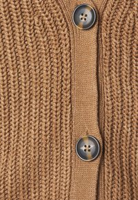 Cardigan en maille de couleur marron chaud avec une texture côtelée. Il présente deux gros boutons foncés à l'avant avec un design marbré subtil.