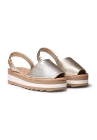 Metalliset kultaiset platform-sandaalit, joissa on avoin varvas, slingback-hihna ja teksturoitu pinta. Ominaisuuksiin kuuluu kerroslatti ja valkoiset sekä ruskeat yksityiskohdat.