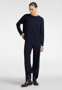 Maglione a maglia blu navy con maniche lunghe e scollo rotondo, abbinato a pantaloni blu larghi. Stivaletti in pelle marrone con suole spesse.