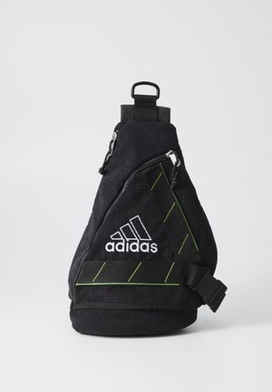 Czarna torba Adidas typu crossbody z białym logo, ukośnymi zielonymi przeszyciami, przednią kieszenią na zamek, regulowanym paskiem i plastikową klamrą na białym tle.
