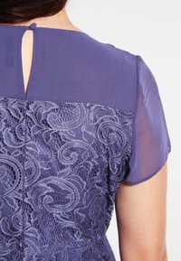 Robe violette avec des manches courtes transparentes et un dos en dentelle à motifs tourbillonnants. Détail en ouverture et bouton au niveau du cou.