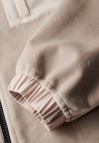 Light beige fabric with soft, smooth texture. Features a gathered cuff with elastic, contrasting inner lining, and a sleek design.
