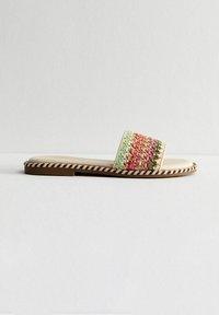 Sandal plana sin talón con una correa de tejido trenzado multicolor texturizado, plantilla beige y suela marrón a rayas.