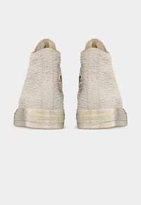 Ζευγάρι κρεμ Converse sneakers με ψηλό πάνω μέρος, υφασμάτινα με υφή και φθαρμένες λαστιχένιες σόλες, εμφανιζόμενα από πίσω.
