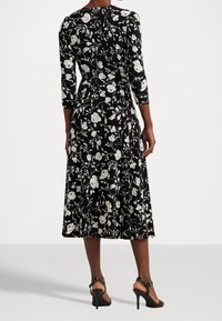 Czarna sukienka w kwiaty z trzema ćwierć rękawami, z białymi wzorami róż, w sylwetce w kształcie litery A i długości do połowy łydki. Zawiera sandały na kostkę.