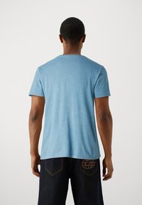 Helles blaues T-Shirt mit kurzen Ärmeln und Rundhalsausschnitt, aus einem weichen, strukturierten Stoff gefertigt. Der Rücken zeigt eine dezente Nahtdetails.