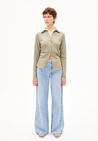 Camicia khaki a maniche lunghe con design a bottone, abbinata a jeans a gamba larga blu chiaro. Texture liscia, stile minimalista, dettagli sottili.