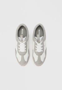 Par hvide og grå Michael Kors sneakers med snørebånd, set ovenfra på en ensfarvet hvid baggrund.