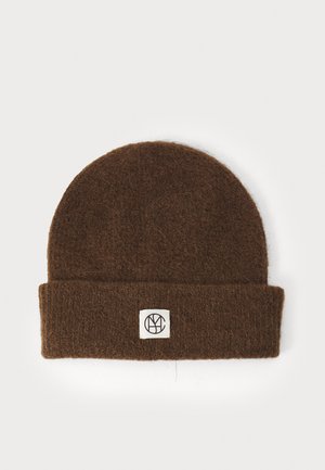Brown wool beanie with a rolled cuff featuring a white square patch displaying a black logo. Soft texture, rounded top shape.