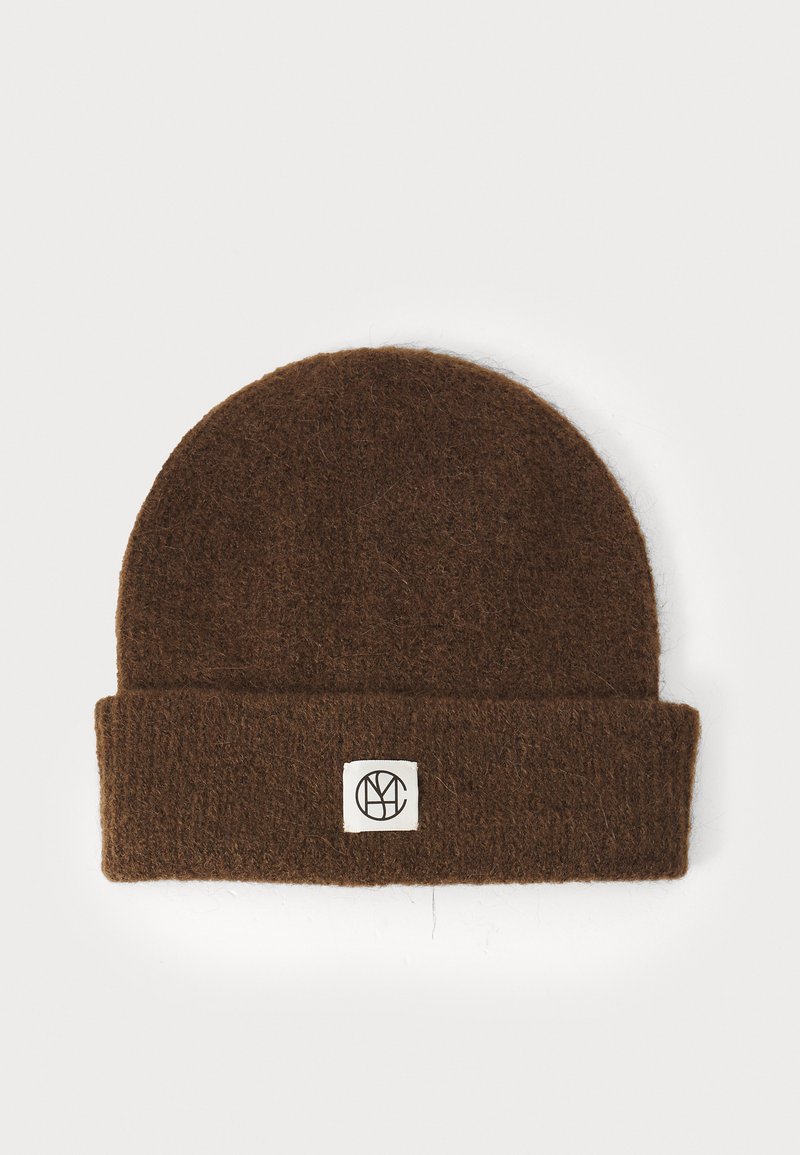 Bonnet en laine marron avec un revers, présentant une boîte blanche avec un logo noir. Texture douce, forme arrondie au sommet.