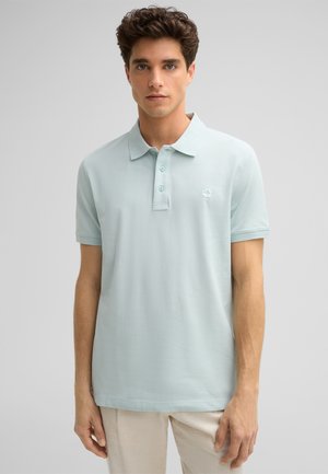 Polo shirt bleu clair en tissu lisse, doté d'un col classique, d'une patte de boutonnage à trois boutons et d'un petit logo brodé sur la poitrine.