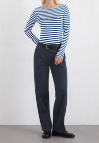 Niebiesko-biała w paski, długie rękawy bluzka z okrągłym dekoltem, połączona z ciemnymi, luźnymi spodniami i czarnymi butami. Prosty detal w postaci paska.