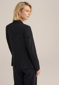Musta kohandatud bleiser, millel on slim fit, kõrvalõige, ühe nupuga sulgemine ja struktureeritud õlad. Sile tekstuuriga kangas.