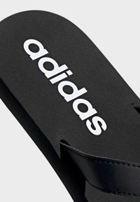 Chancla de goma negra con el logo blanco de "adidas". Cuenta con una plantilla texturizada, una sola tira negra y bordes curvados.