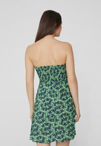 Schulterfreies Kleid mit einem geschmückten Oberteil, das ein grünes und blaues tropisches Blättermuster aufweist, aus leichtem Stoff gefertigt.
