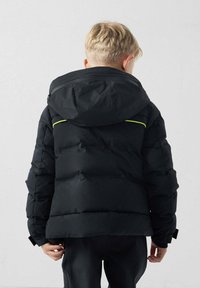 Chaqueta acolchada negra con capucha, textura acolchada y detalles en amarillo neón en la espalda y los hombros. Cuenta con un bolsillo con cremallera.