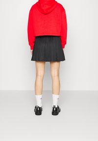 Czerwony krótki hoodie, czarna plisowana spódnica, białe skarpety w falbanki i czarne buty. Skup się na intensywnych kolorach i kontrastujących fakturach.