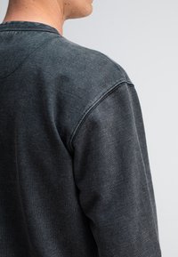 Donkergrijze sweatshirt met een ronde hals, textuurstof en zichtbare stiksels langs de schouders, met een relaxed fit.