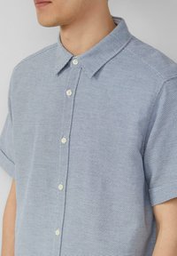 Kurzärmliges Hemd mit Knöpfen in Hellblau aus strukturiertem Stoff, dezentem weißen Muster und klassischem Kragen. Fünf weiße Knöpfe an der Vorderseite.