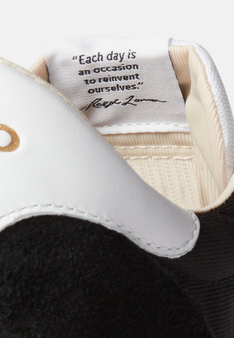 Baskets noir et blanc avec des matériaux texturés, présentant un dessus noir doux, des accents en cuir blanc et une doublure intérieure beige avec une citation imprimée.